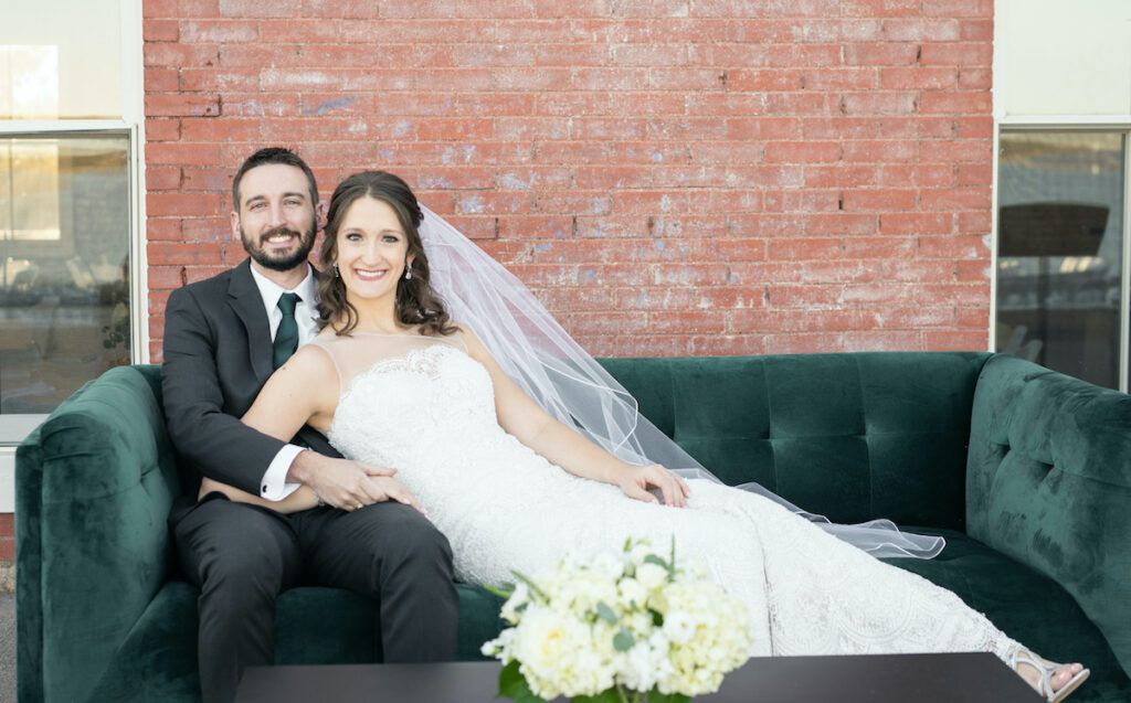 Bride and groom are sitting on a green couch rented for the wedding reception.