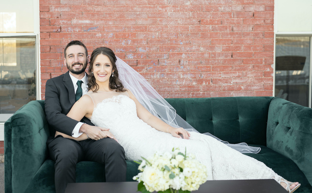 Bride and groom are sitting on a green couch rented for the wedding reception.